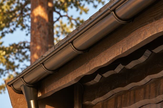 Black metal gutter and downspout on a wood-sided home